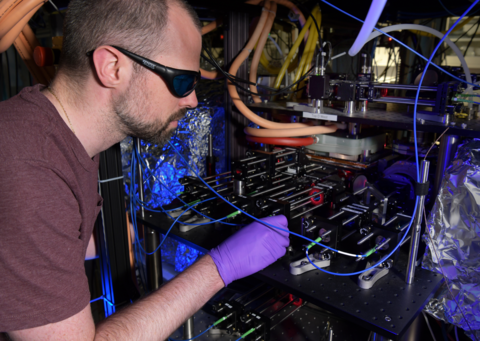 Dan Barker wears dark safety glasses as he peers into the complex CAVS apparatus in a darkened lab. 
