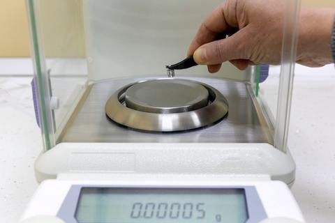 A scientist (doctor or pharmacist) weighs a small metal object on an accurate analytical balance.