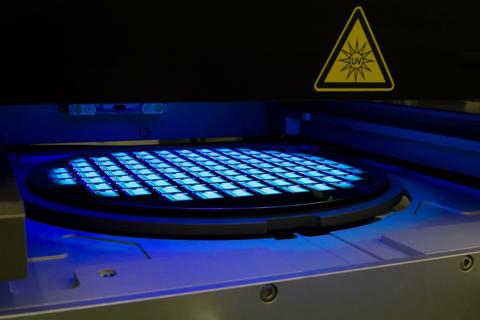 Photograph depicting IC manufacturing showing glowing squares on a round wafer, with a yellow triangular warning indicator labeled UV.