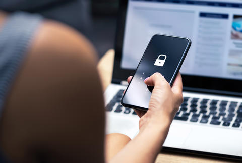 Person holding a cell phone in front of a laptop computer 