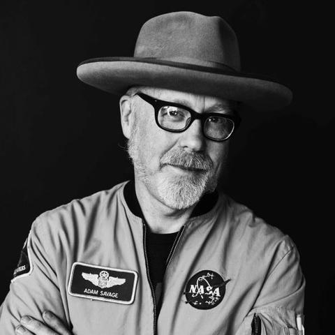 Black and white headshot of a man wearing glasses and a hat with a NASA jacket