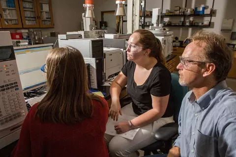 Three NIST staff members sitting together in front of the computer monitor of a GC-MSMS instrument. They are looking at mass spectral data. 