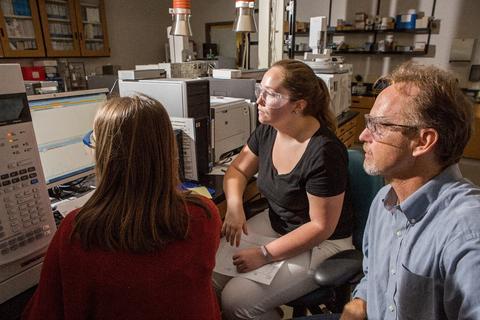 Three NIST staff members sitting together in front of the computer monitor of a GC-MSMS instrument. They are looking at mass spectral data. 