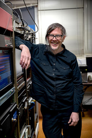 Andrew Novick poses leaning on a rack of servers and other electrical equipment.