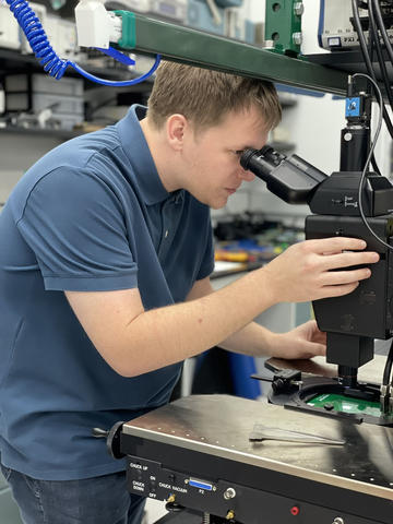 Drew Borders leans forward to look into a microscope attached to a large frame.