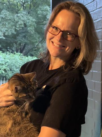 Kate Beers poses for a casual photo, smiling and holding a cat. 