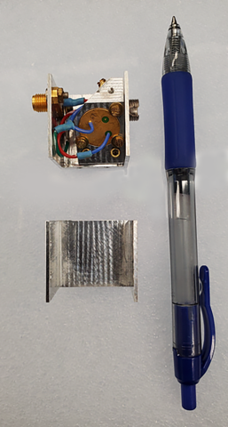 A square device with wiring inside is taken apart for viewing with a pen laid alongside for scale. 