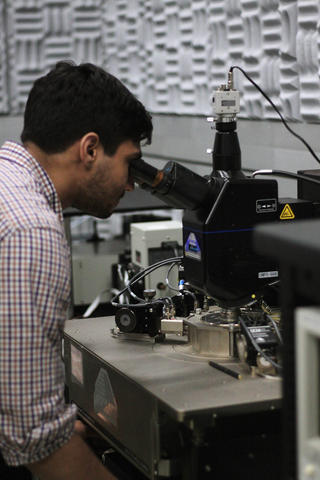 Samuel Márquez González leans forward to look through a microscope in the lab. 