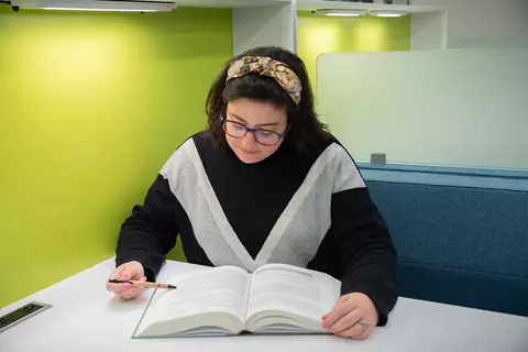 Kathryn Miller sits reading a book at a small table in the NIST library. 