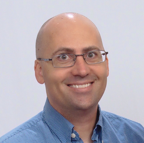 Headshot of a bald man wearing glasses and a blue collared shirt