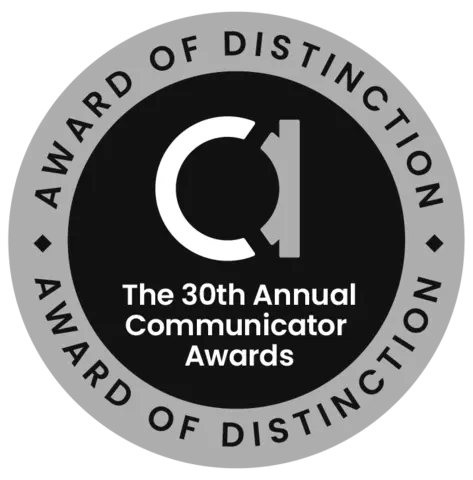 Circle badge. Silver exterior ring with writing at top and bottom: Award of Distinction. Black interior. Lowercase letter A. Words: The 30th Annual Communicator Awards