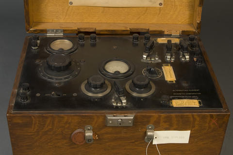 Magnetic comparator device for testing prison bars, circa 1930s. The device is framed in a wooden box that doubles as a carrying case. The interior of the box has a control panel with various settings knobs.