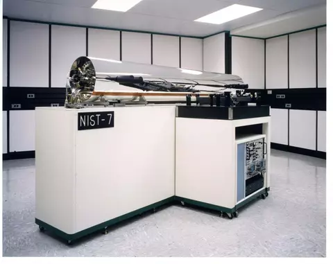 A large shiny silver-colored cylinder is mounted on white cabinetry with a sign saying "NIST-7."