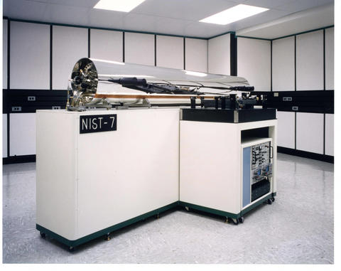 A large shiny silver-colored cylinder is mounted on white cabinetry with a sign saying "NIST-7."