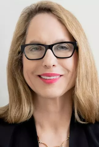 Woman with shoulder length blond hair, black jacket and black glasses