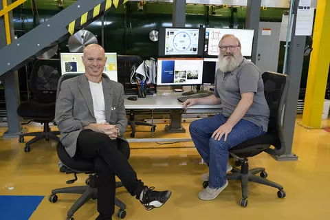 NIST researchers sit in chairs next to each other at NIST's Gaithersburg campus, with computers and technical equipment in the background.