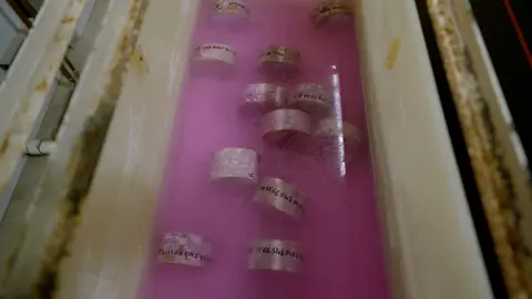 Labeled concrete samples lay in pink liquid inside a trough. 