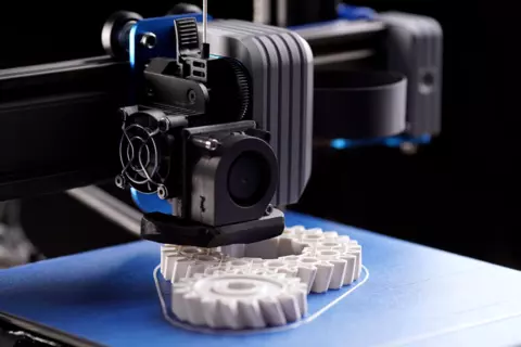 a 3D printer prints white gears using material extrusion