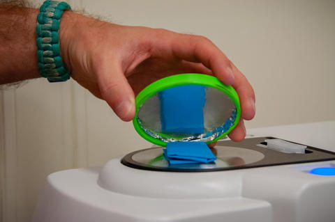 A close-up shot of hand holding a circular lid over a piece of blue clothing on top of a scientific device.
