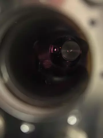 View through a circular opening into a dark interior. A red dot floats in the darkness. 