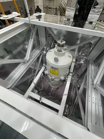 A cylindrical tank is held with struts inside a square scaffold in a lab. 