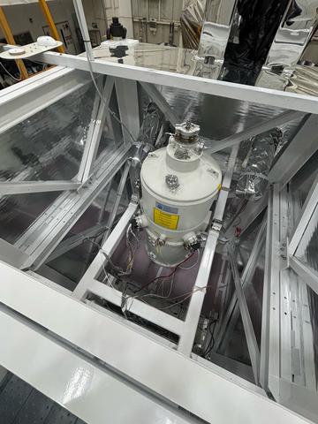 A cylindrical tank is held with struts inside a square scaffold in a lab. 