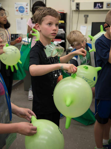 child holding a green balloon in a room with other children