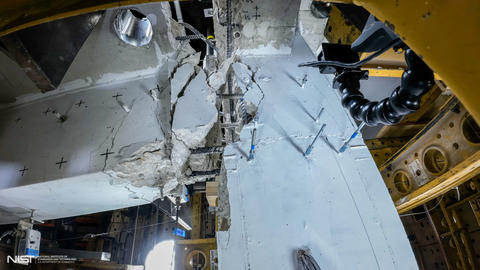 Close-up view of connection point shows concrete beam broken away from slab and exposed rebar.