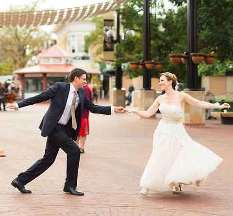 A man and woman, wearing wedding clothes, dancing in an outdoor setting. 