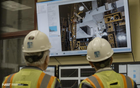 Two people in hard hats, shown from behind, look at a large screen showing concrete slabs and testing equipment.