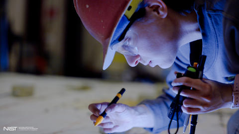 Close-up shows a female researcher in a hard hat looking down, shining a flashlight and holding a marker.