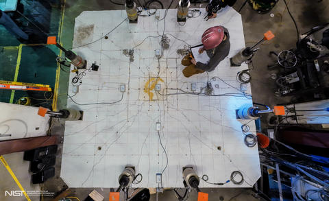 An overhead view shows a researcher in a hard hat making notes while kneeling on a concrete slab surrounded by scientific equipment.