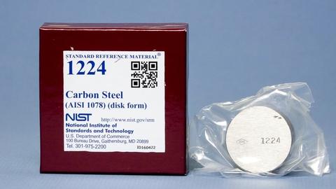 image of a brown box with a label that reads Standard Reference Material 1224 and a silver metal disk next to it with a stamped numbers 1224 on the disk