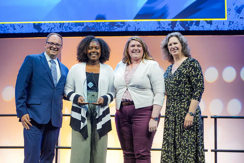 A group of four individuals stand on a stage, posing for a photo with an award.