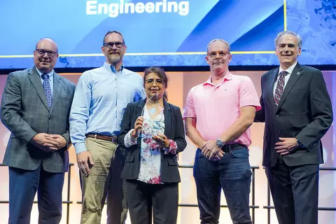 A group of people stand on stage, posing for a photo with an award.