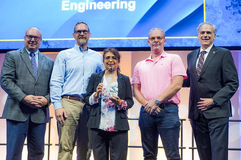 A group of people stand on stage, posing for a photo with an award.
