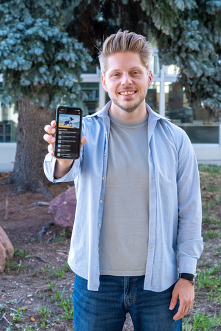 Bill Fisher smiles as he poses holding out a smartphone that shows a mobile driver's license. 
