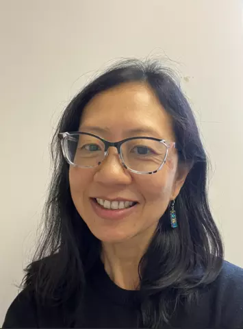 A woman with long black hair and glasses, smiling for a photo. 