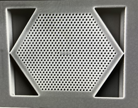 Close-up view of a hexagon shape with rows of tiny holes filling it. 