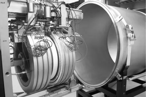 Figure 1. NIST 500 mm diameter guarded-hot-plate apparatus: plate and edge guard (foreground), vacuum bell jar (background). The edge guards are partially separated revealing a white insulation specimen.