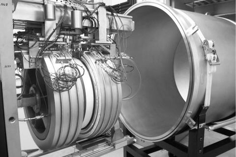 Figure 1. NIST 500 mm diameter guarded-hot-plate apparatus: plate and edge guard (foreground), vacuum bell jar (background). The edge guards are partially separated revealing a white insulation specimen.