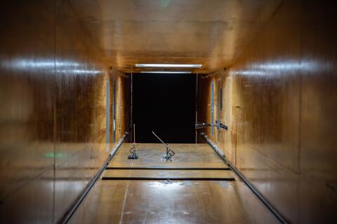 View from inside a square tunnel looking out into a dark space. Near the end of the tunnel, two small devices are attached to the floor. 