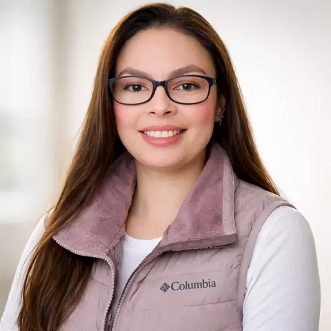 Professional headshot of Viviana Faride Dovale Farelo, a woman with long brown hair, smiling, wearing glasses, a white shirt and purple vest.