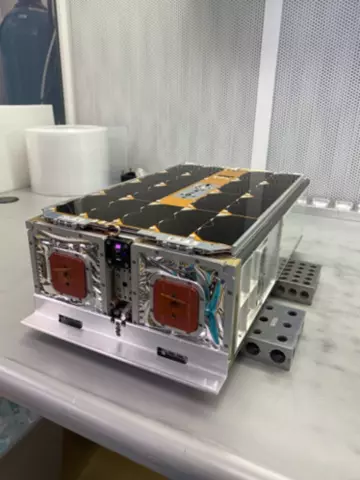 A rectangular device with wiring and various connections sits on a metal lab table. 