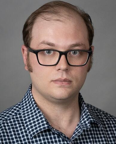 Aaron Rowane, a man with short hair and glasses, posing for a professional headshot. 