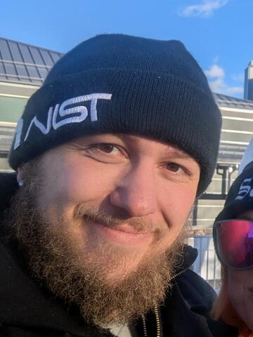 Headshot of Austin Gerlt, a man with a beard, smiling, wearing a NIST beanie.