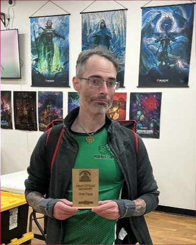 A man poses holding an award plaque in a room decorated with card and board gaming artwork. 