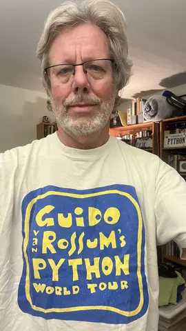 Guido van Rossum poses in a vintage T-shirt that reads: Guido van Rossum's Python World Tour.
