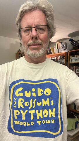 Guido van Rossum poses in a vintage T-shirt that reads: Guido van Rossum's Python World Tour.