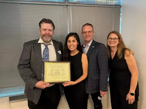 A group of four business professionals pose for a group photo honoring Polette Centellas, center, holding up her award plaque.